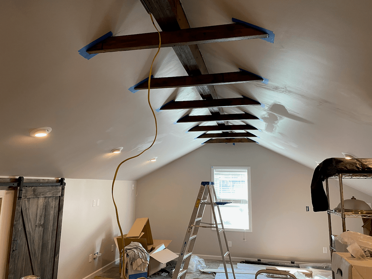 Vaulted attic bedroom in progress with exposed stained beams and a barn door