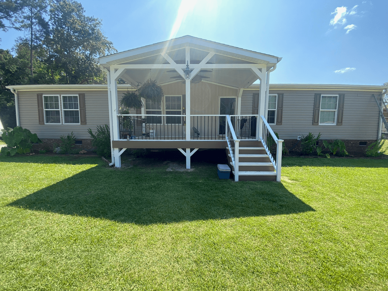 Gabled front porch addition with railings and steps on a sunny lawn