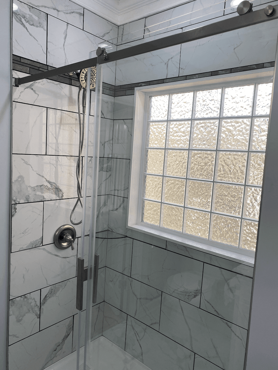 Marble-look tile shower with frameless glass door and glass-block window